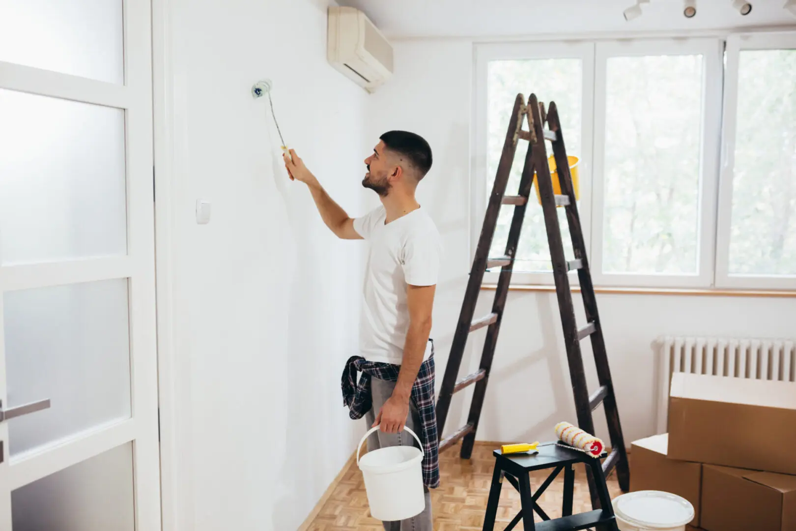 young man painting indoor wall with roller